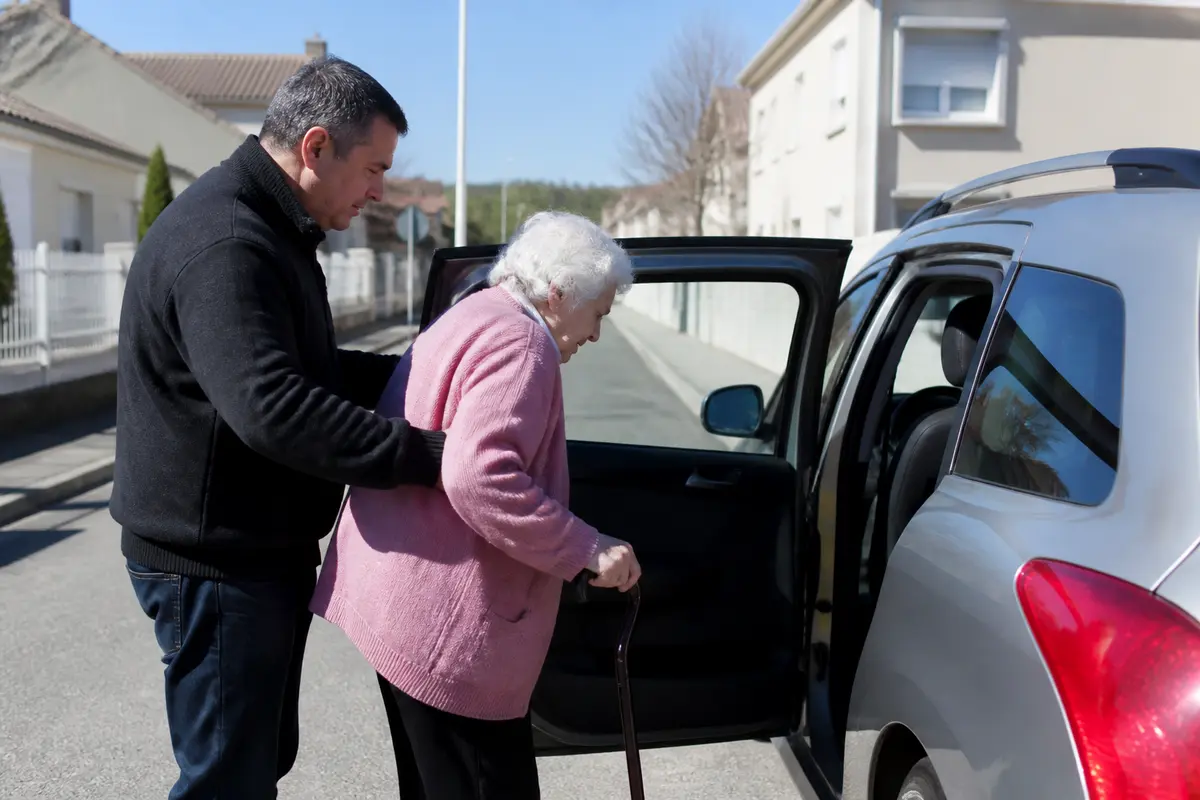 Homme aidant une femme âgée à entrer dans une voiture pour accompagnement personnalisé