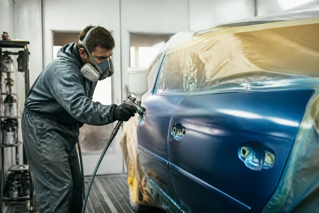 Carrossier appliquant une peinture bleue sur portière, évoquant le salaire en peinture automobile