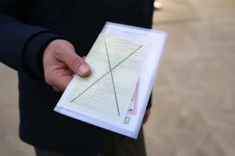 Main tenant une carte grise barrée, prête pour vente ou transfert véhicule.