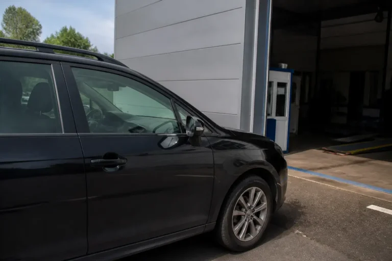 Voiture noire attend contrôle technique dépassé mais prévue avec rendez-vous près d’un garage.